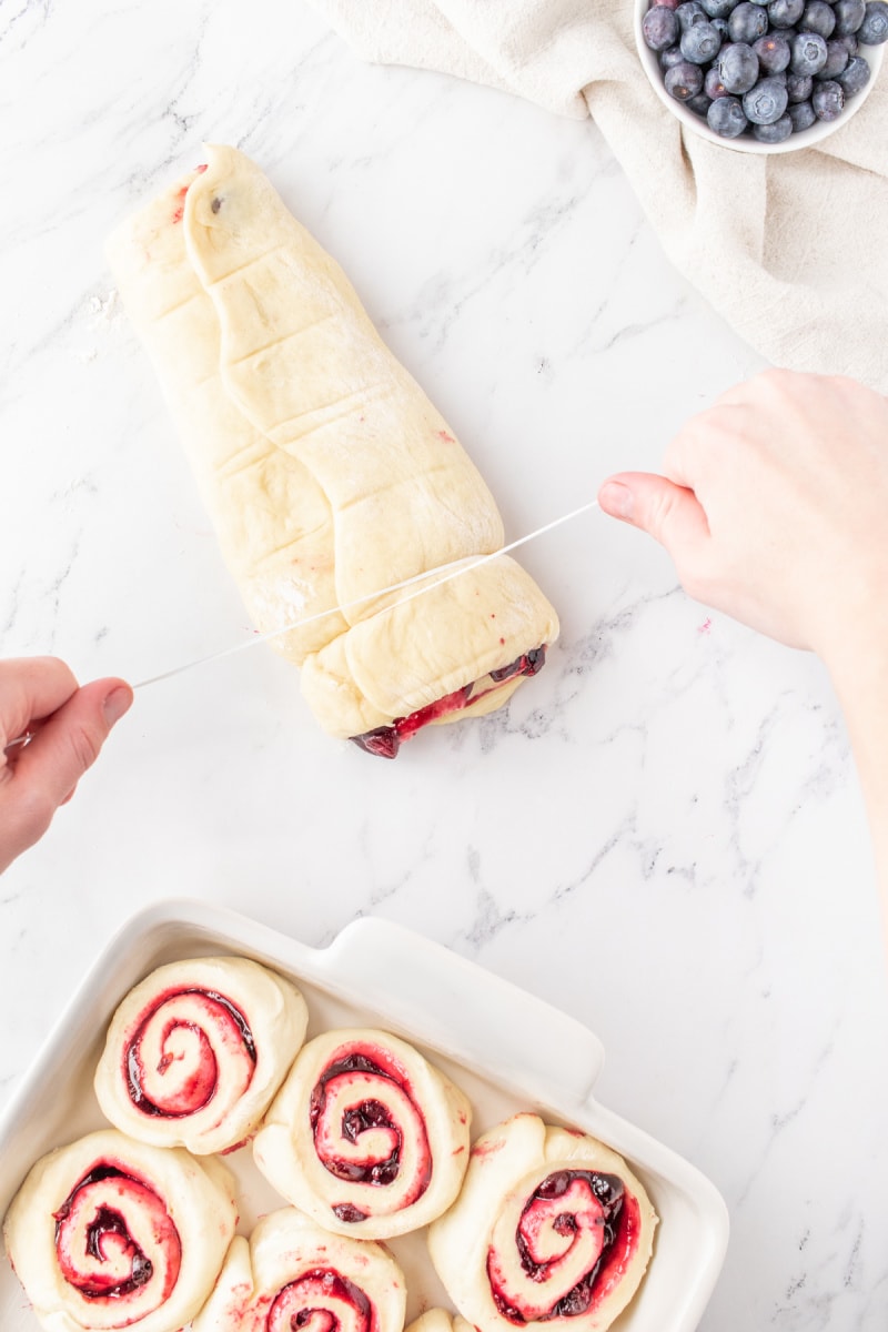 rolled blueberry sweet rolls and showing using dental floss to cut