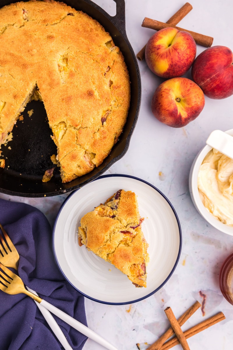 slice of cast iron peach cornbread on plate with the rest in a cast iron skillet