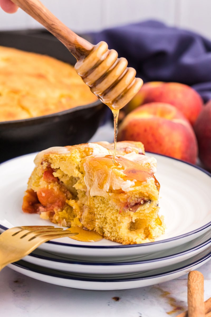 dripping honey onto slice of cast iron peach cornbread on plate