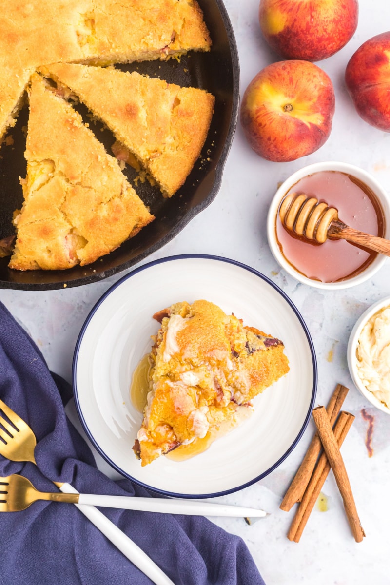 slice of cast iron peach cornbread on plate with rest in cast iron skillet