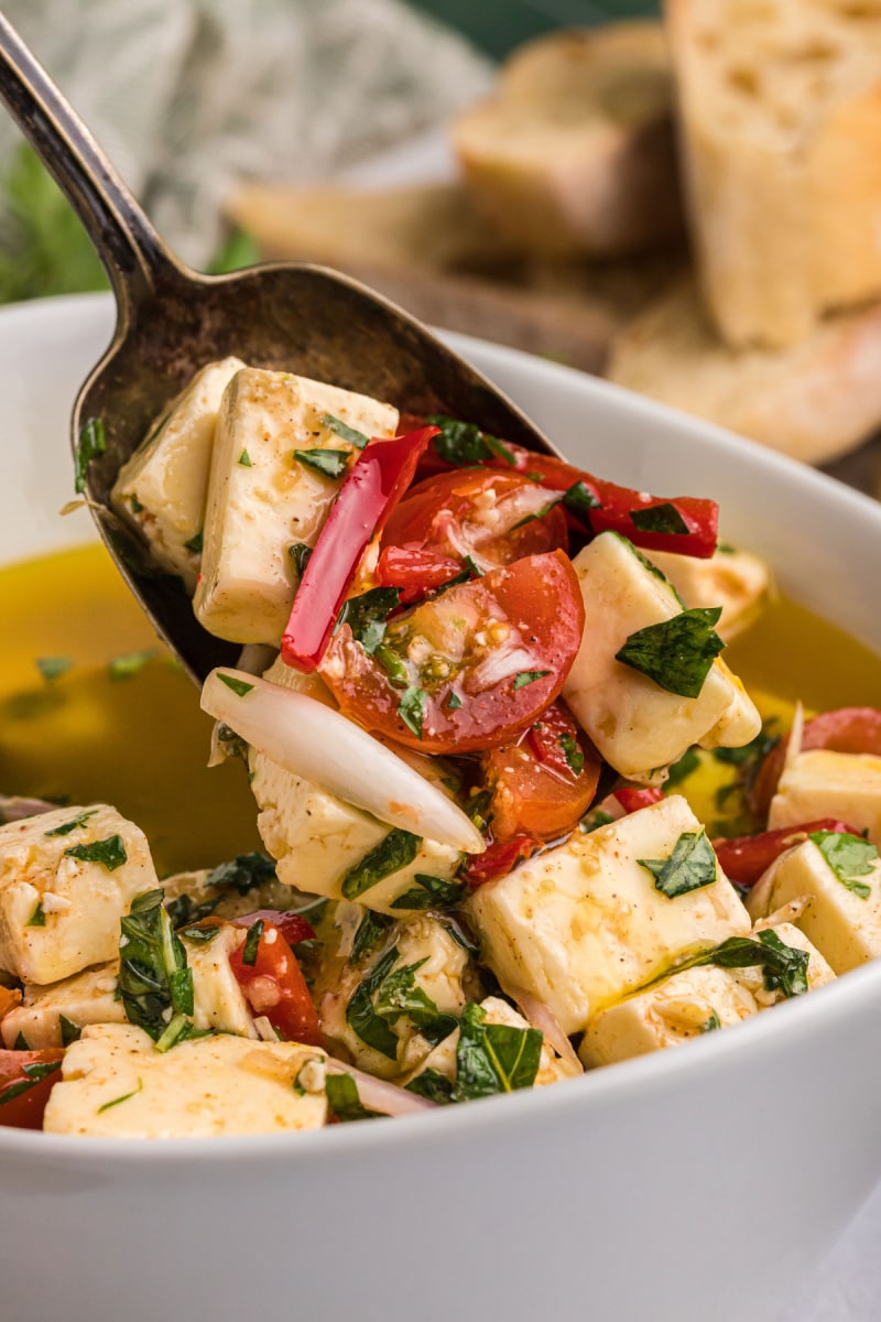 spoon in dish of marinated feta with cherry tomatoes