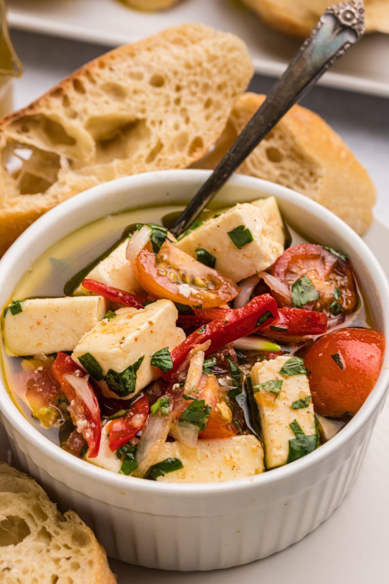 spoon in dish of marinated feta with cherry tomatoes