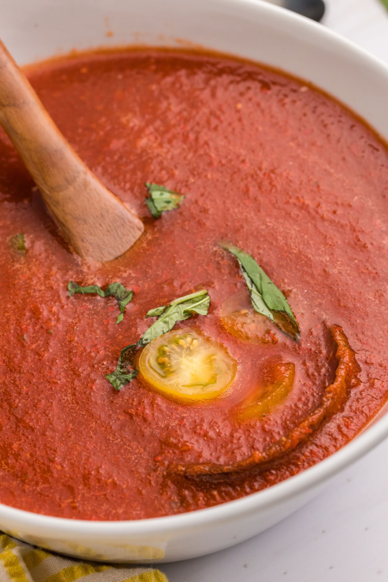 spoon in bowl of chilled tomato soup with tomato and basil garnish