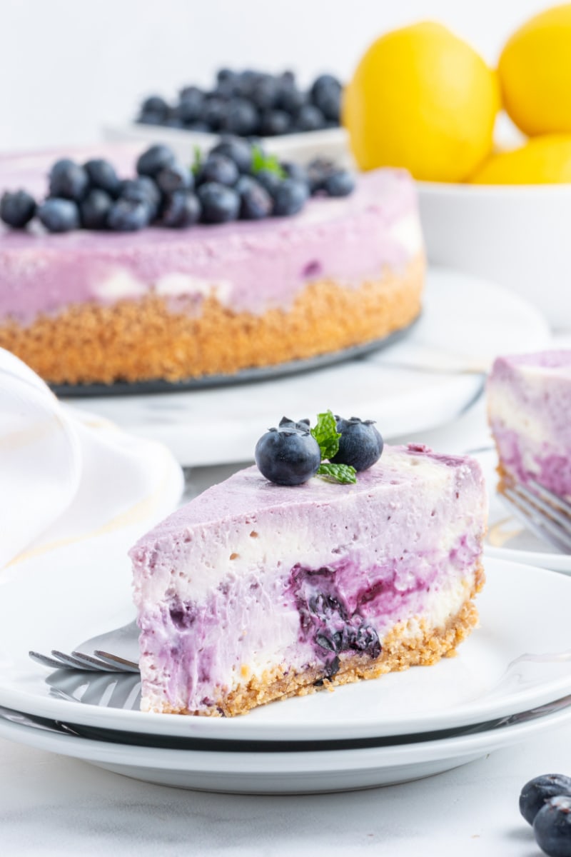 slice of blueberry lemon cheesecake on plate with whole cheesecake in background