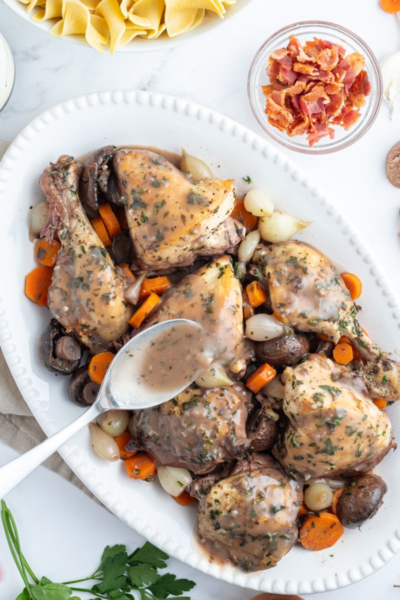 spooning gravy onto coq au vin on platter