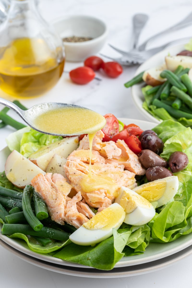 spooning dressing onto salmon nicoise salad