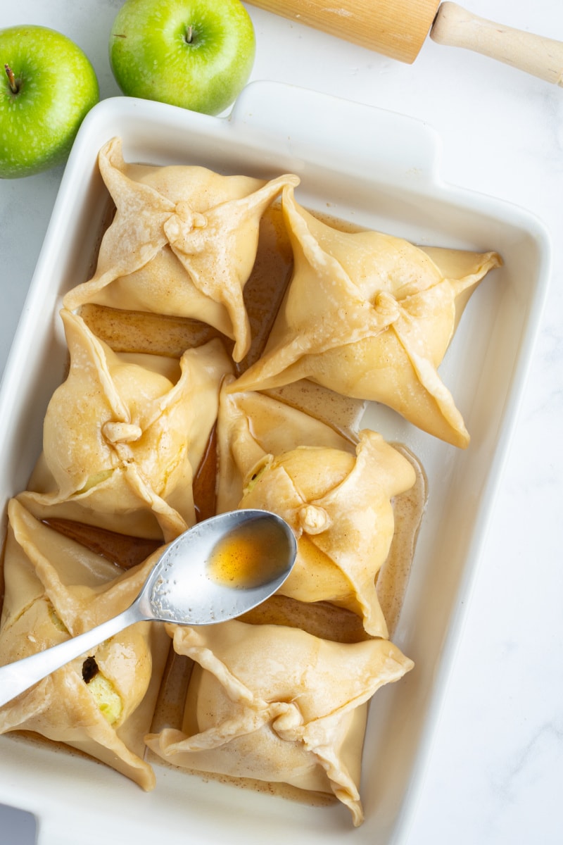 spooning sugar syrup onto apple dumplings in baking pan