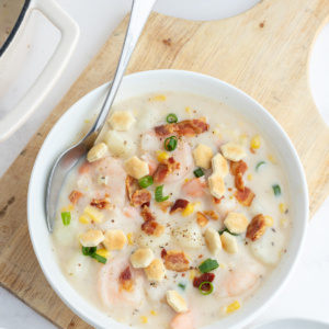 bowl of corn and shrimp chowder with spoon and bacon on top