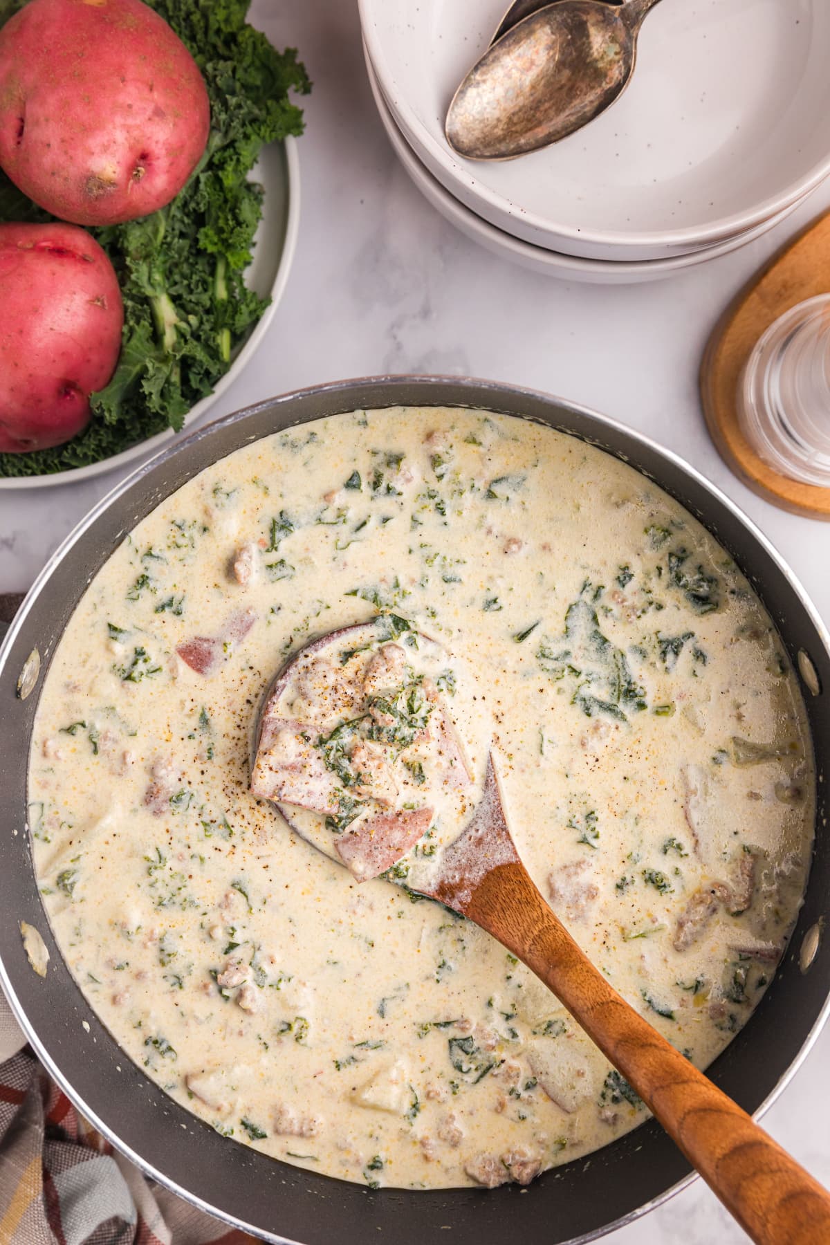 overhead shot of potato sausage and kale soup with wooden spoon in pan