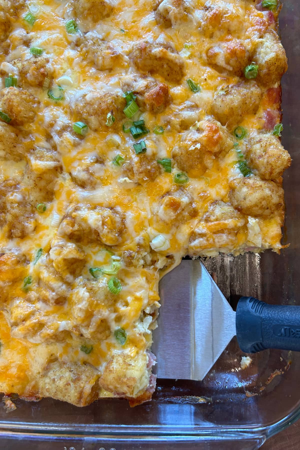 tater tot breakfast casserole in dish with spatula taking out serving