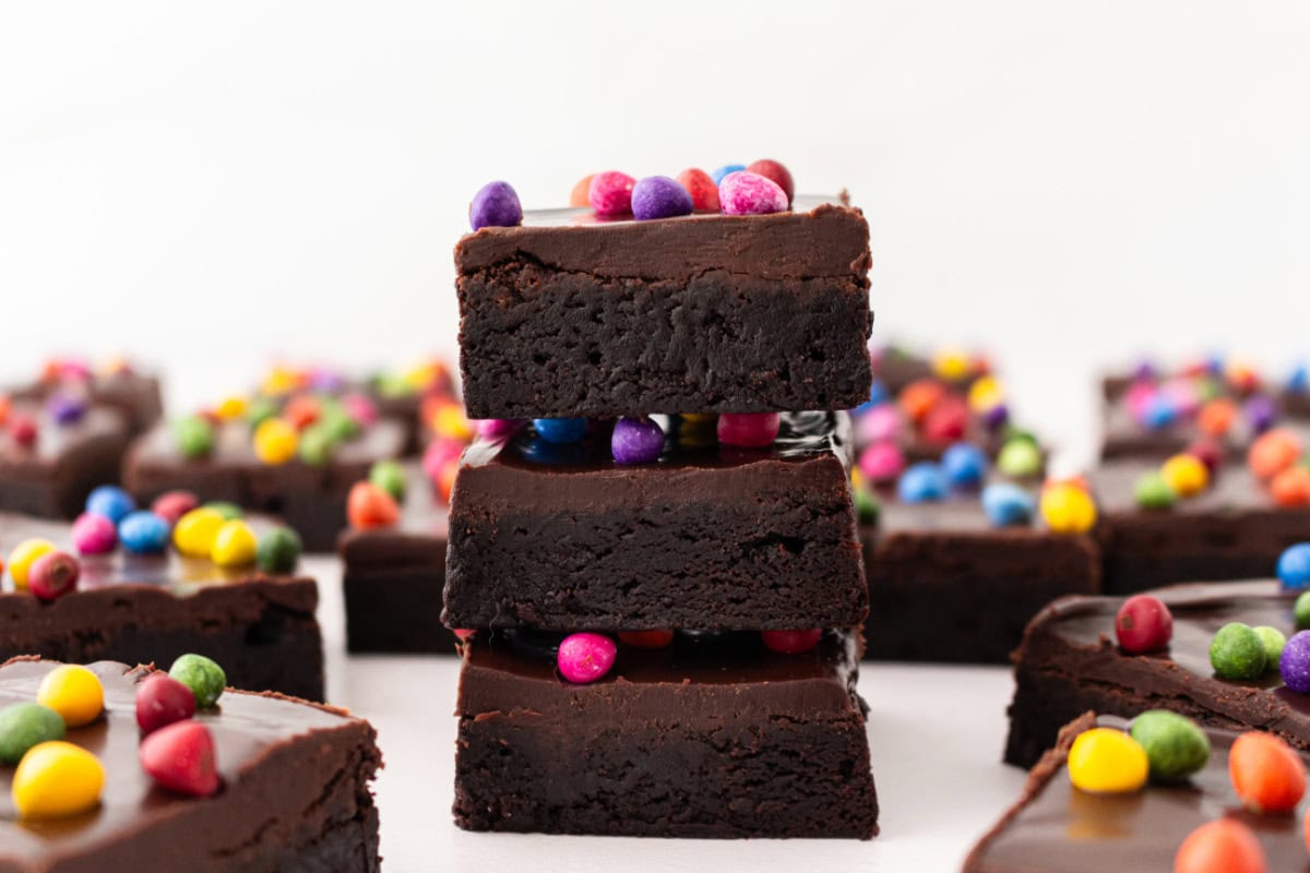 Cosmic Brownies are a fudgy, chocolatey copycat of the classic treat with ganache and colorful candy-coated chips. Easy and nostalgic! three cosmic brownies stacked