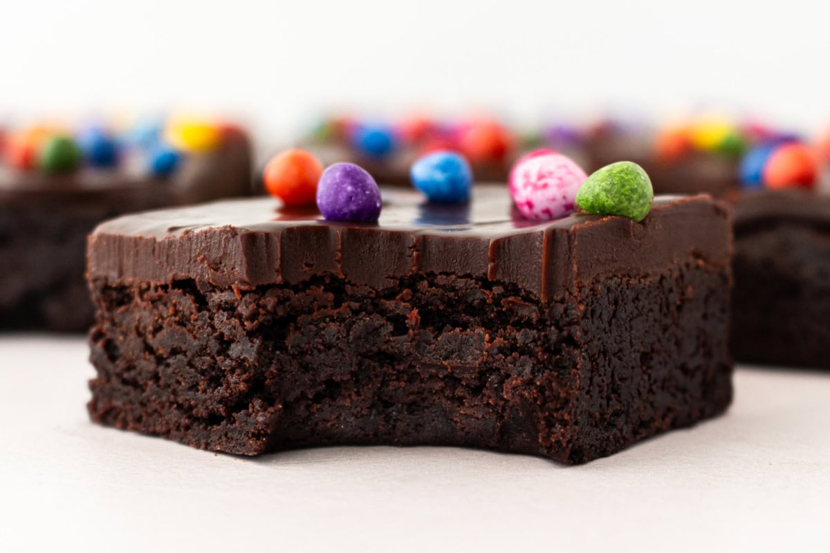 Cosmic Brownies are a fudgy, chocolatey copycat of the classic treat with ganache and colorful candy-coated chips. Easy and nostalgic! cosmic brownie with bite taken out of it