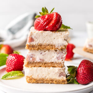 three strawberry cheesecake bars stacked on plate