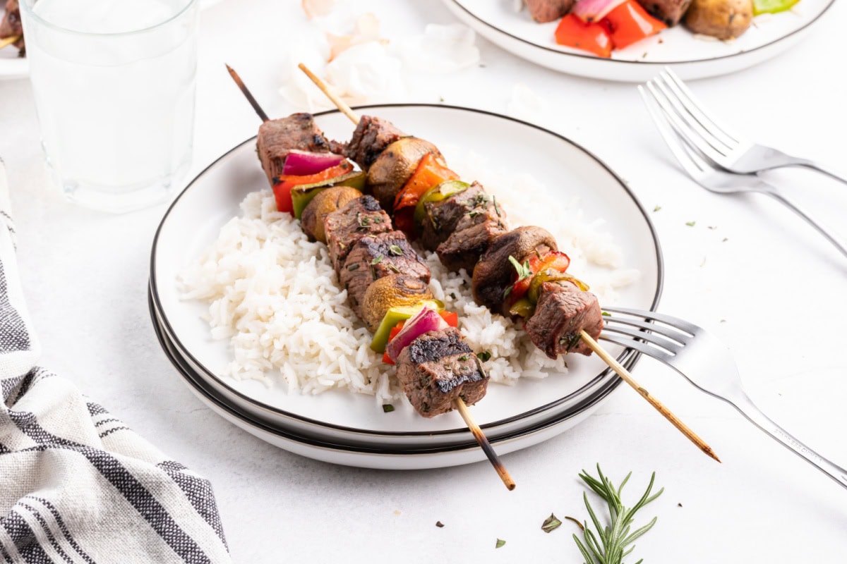 two steak kabobs on a plate with rice