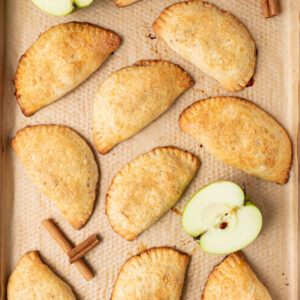 apple hand pies on baking sheet with apples and cinnamon