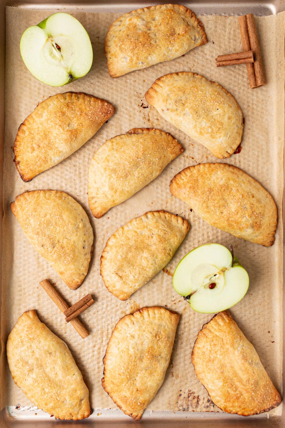 apple hand pies on baking sheet with apples and cinnamon