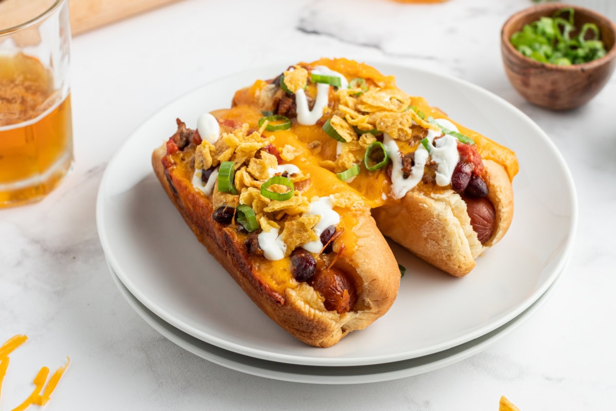 two baked chili dogs on a plate with a beer