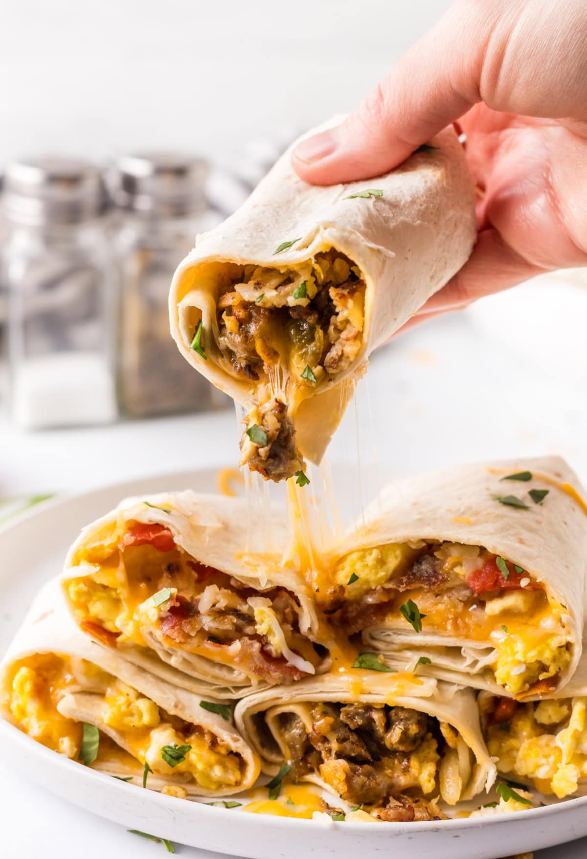 How to make Breakfast Burritos recipe from RecipeGirl.com : scrambled eggs, sausage, hash browns and cheese hand picking up breakfast burrito