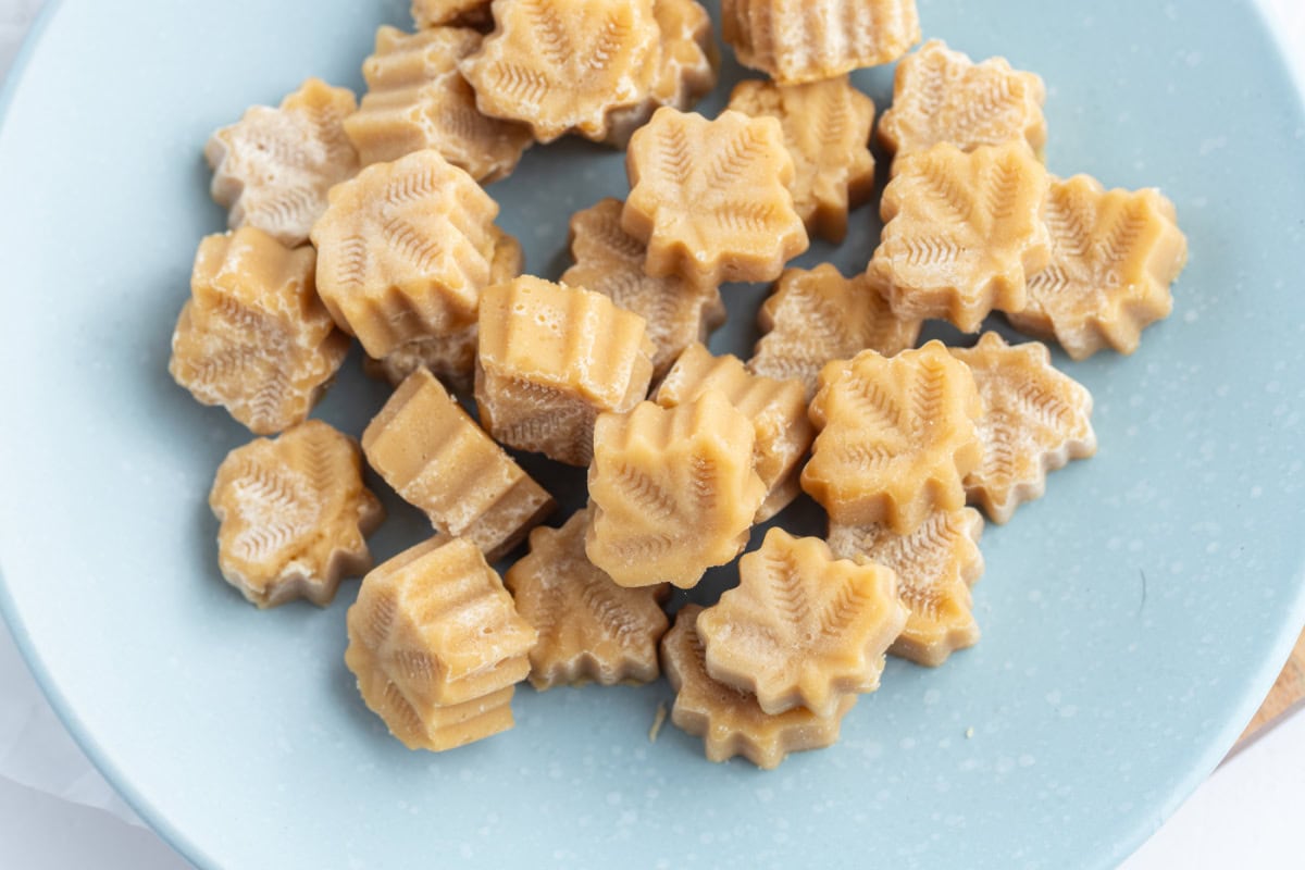 These Maple Syrup Candies are made with only one ingredient: pure maple syrup! Make them in maple leaf molds for cute results. Recipe from RecipeGirl.com. several pieces of maple candy on blue plate