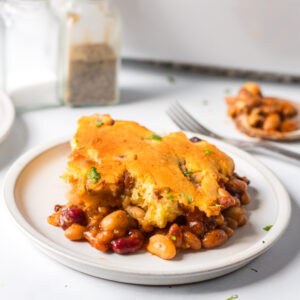 Serving of beans and cornbread casserole with melted cheese and herbs.