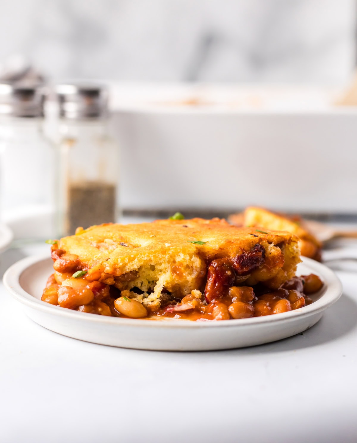Cowboy Casserole is a hearty, baked beans and cornbread casserole full of smoky, sweet, and savory flavor — perfect for cozy family dinners or potlucks! Recipe from RecipeGirl.com. serving of cowboy casserole on plate
