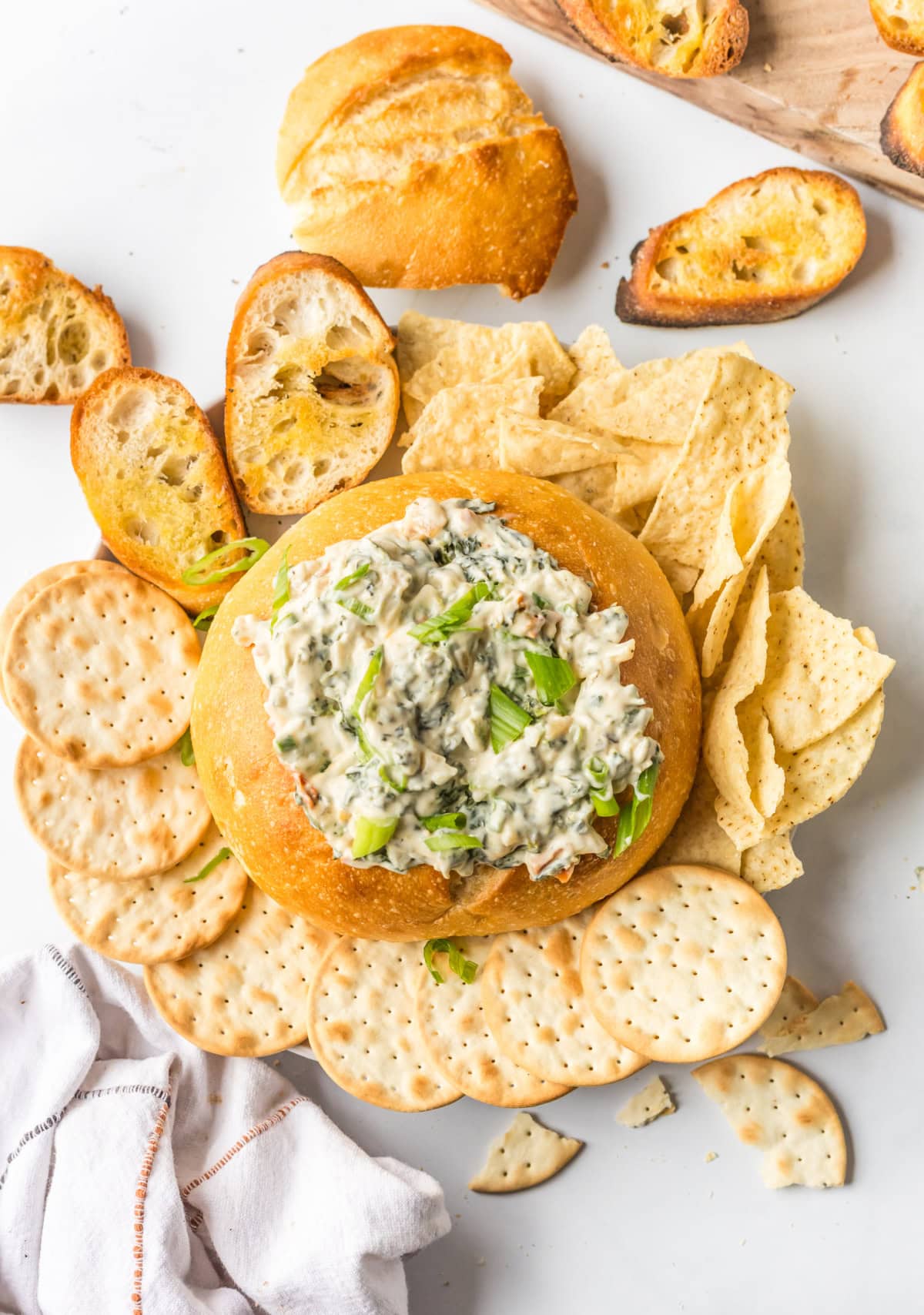 This Knorr Spinach Dip in a bread bowl is creamy, classic, and easy! A timeless appetizer perfect for holidays, game day, or parties. Recipe on RecipeGirl.com. knorr spinach dip recipe in bread bowl surrounded by bread and crackers