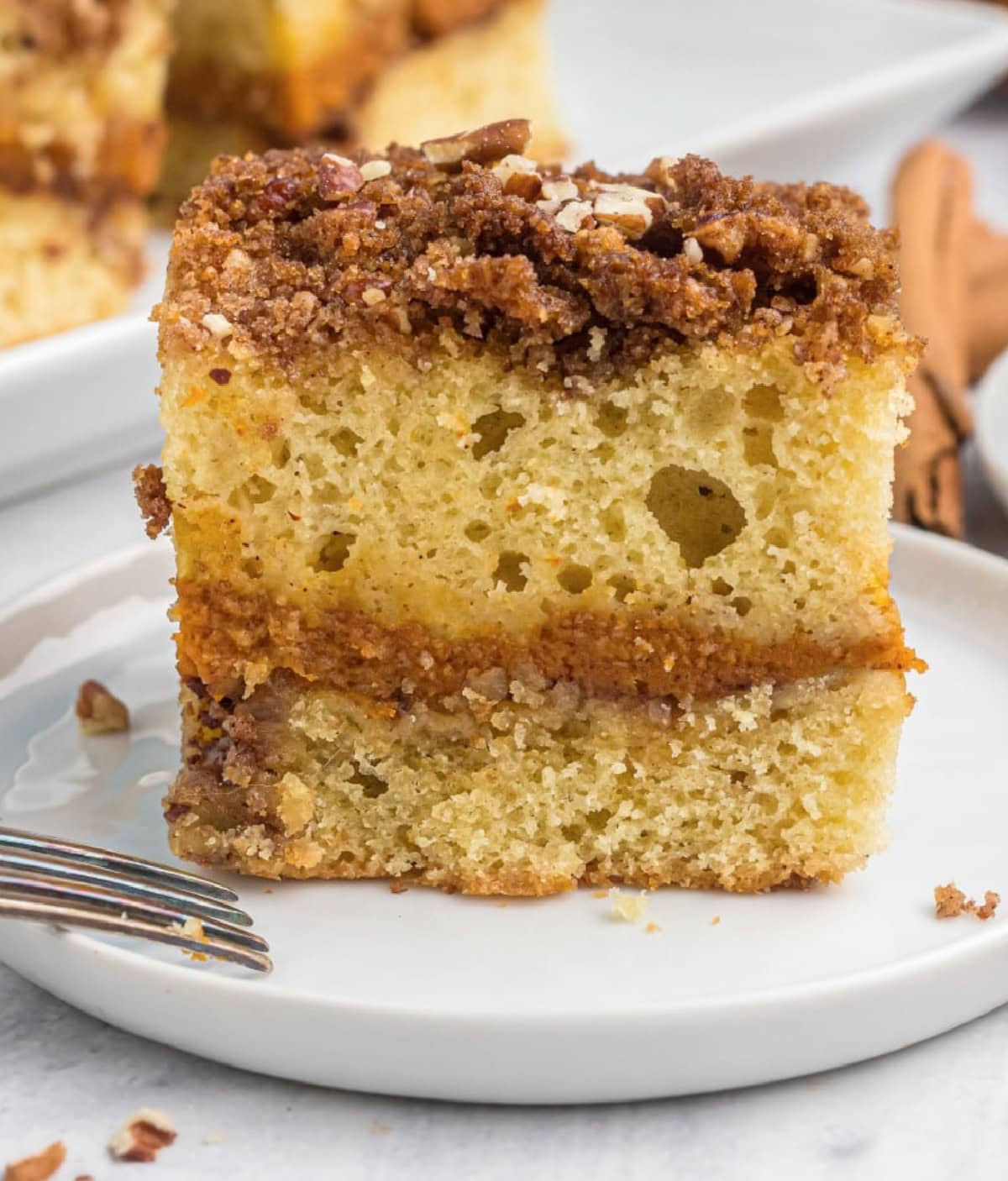 Pumpkin Coffee Cake is a coffee cake with a pumpkin pie filling in the middle and a buttery streusel on top. slice of pumpkin coffee cake on a plate