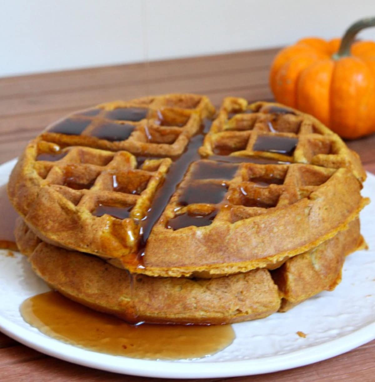 Pumpkin Waffles are crispy homemade pumpkin waffles loaded with pumpkin pie spice and drizzled with pure maple syrup. two pumpkin waffles stacked on a plate with syrup