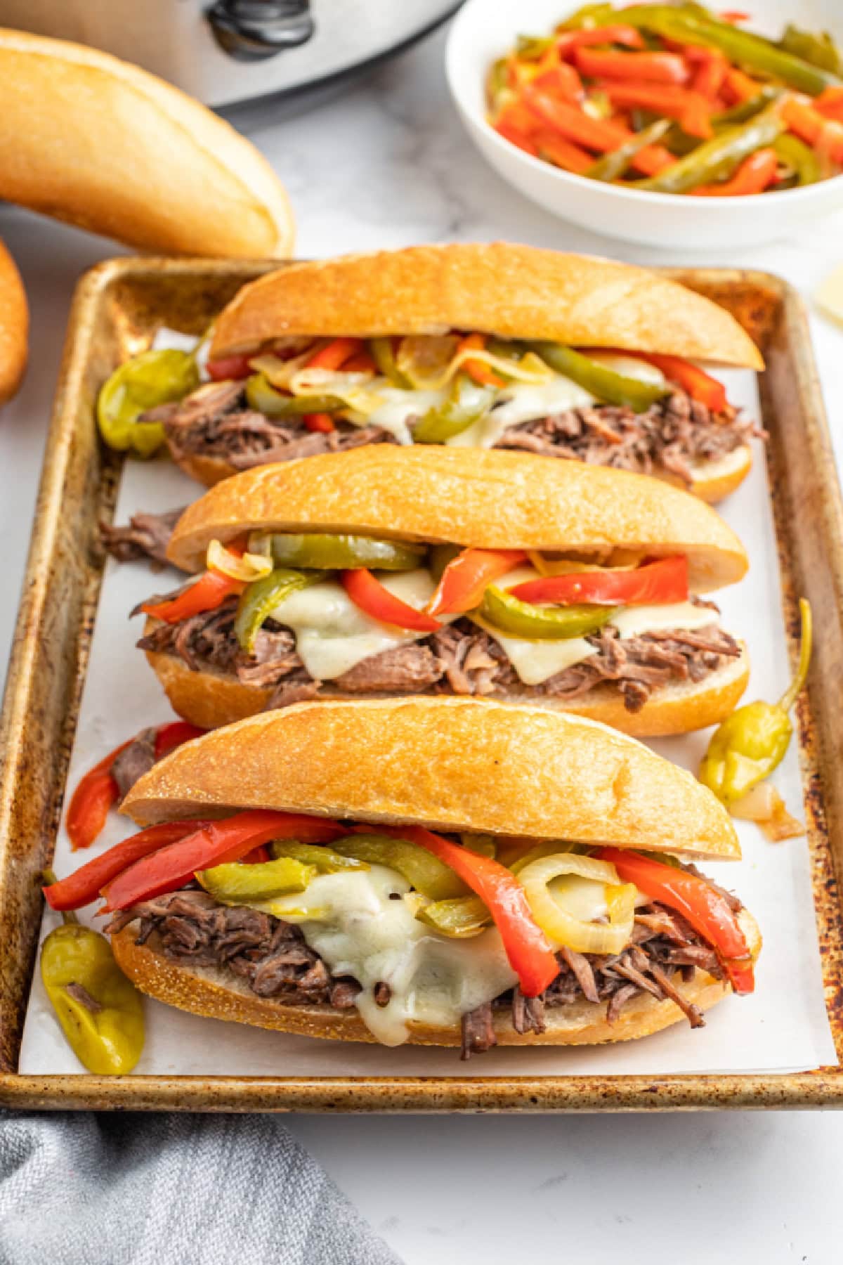 Slow Cooker Italian Beef Sandwiches are the best sandwiches ever. The beef is cooked with pepperoncini and Italian dressing, then shredded. Recipe from RecipeGirl.com. three slow cooker italian beef sandwiches on a baking sheet