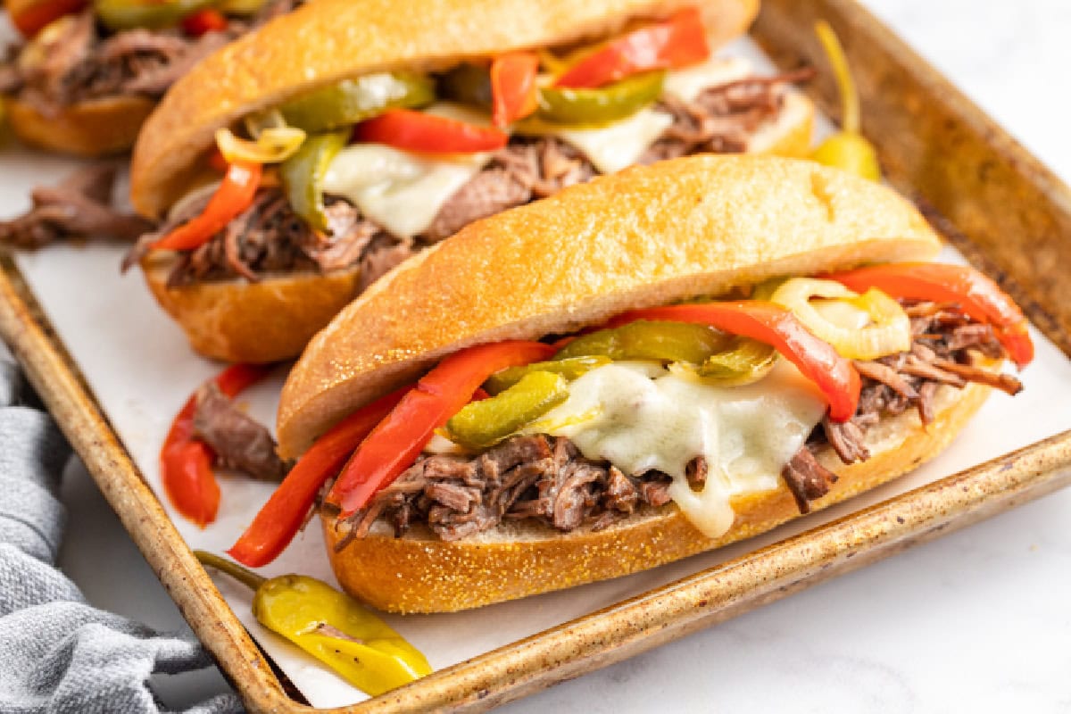 Slow Cooker Italian Beef Sandwiches are the best sandwiches ever. The beef is cooked with pepperoncini and Italian dressing, then shredded. Recipe from RecipeGirl.com. slow cooker italian beef sandwiches on a baking sheet