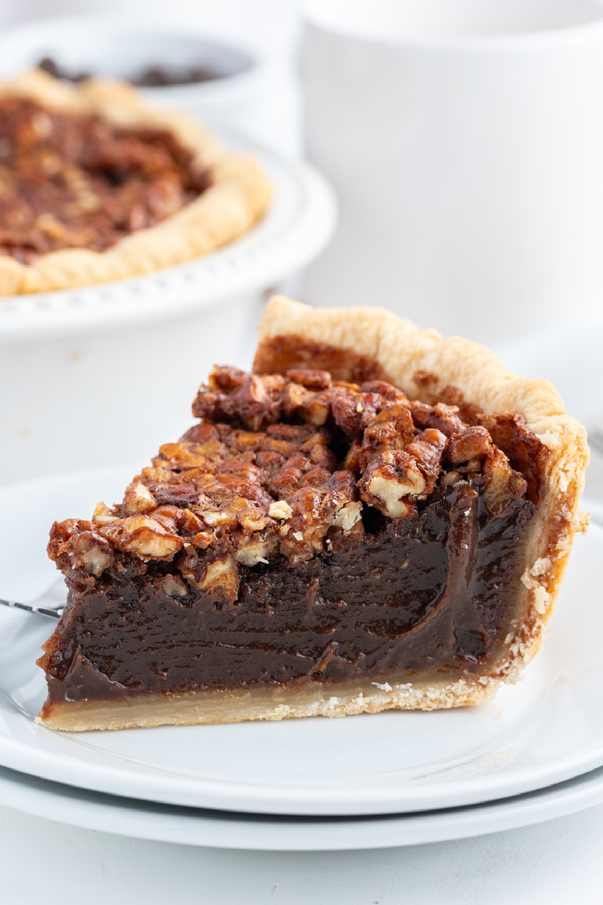 Rich Bourbon Chocolate Pecan Pie made with dark corn syrup, brown sugar, melted chocolate, and toasted pecans. A decadent holiday dessert that’s unforgettable! slice of bourbon chocolate pecan pie on a plate