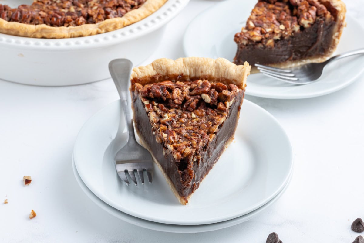 Rich Bourbon Chocolate Pecan Pie made with dark corn syrup, brown sugar, melted chocolate, and toasted pecans. A decadent holiday dessert that’s unforgettable! slice of bourbon chocolate pecan pie on a plate with a fork
