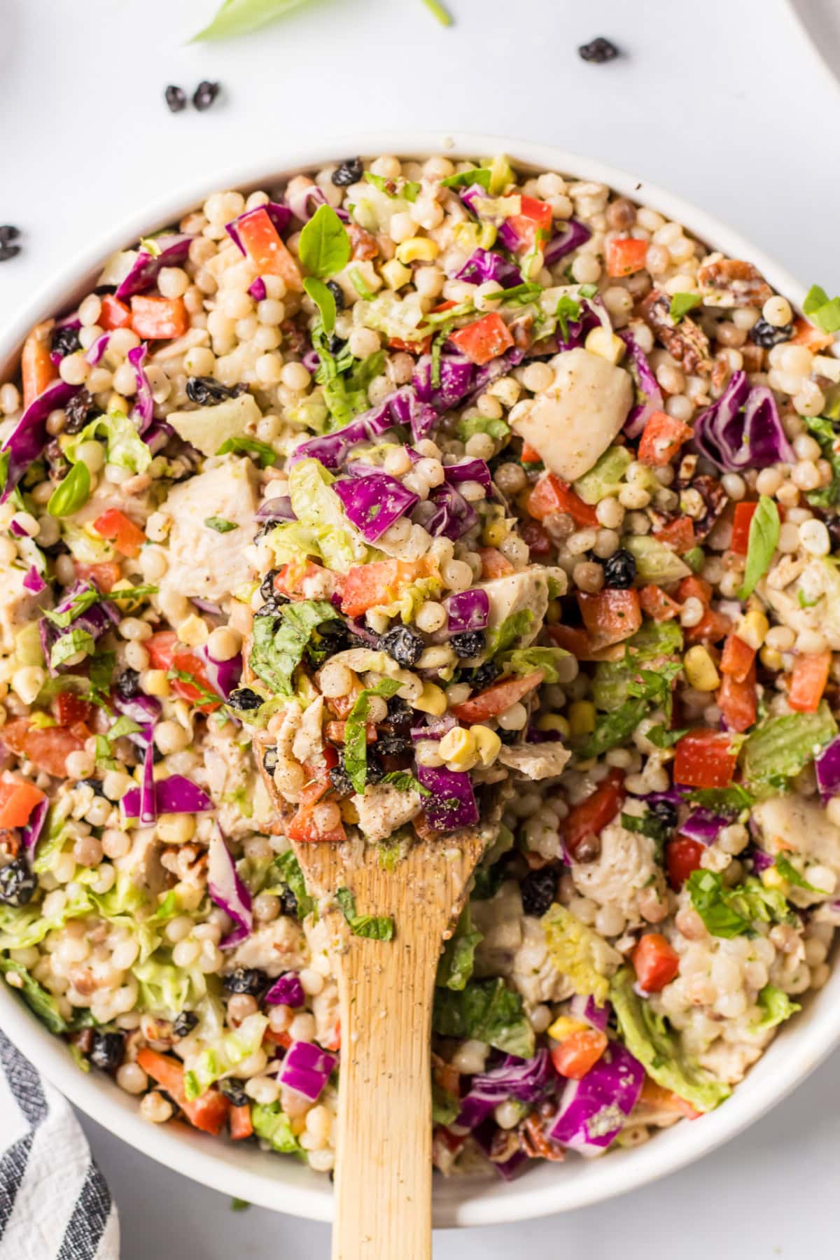 This Chopped Chicken and Couscous Salad with Sweet Basil Dressing is fresh, flavorful, and flexible! Swap turkey, wild rice, and cranberries for a fall twist. bowl of chopped chicken and couscous salad with spoon