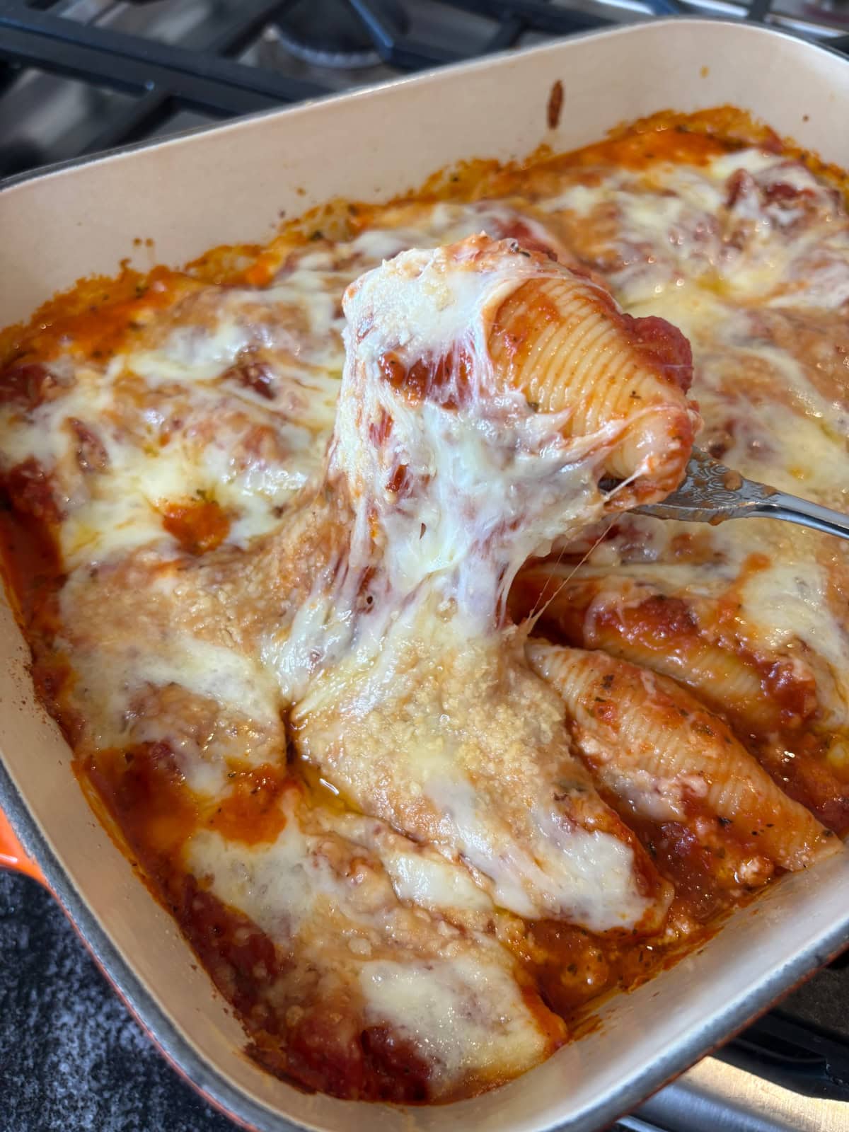 These cheesy stuffed shells from Ree Drummond’s The Essential Recipes cookbook are baked with marinara and four kinds of cheese. Pure, bubbling comfort! spoon taking stuffed shell out of pan with cheese pull