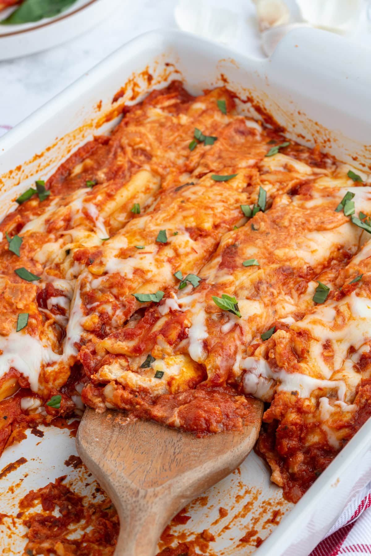 This classic Cheese Manicotti is stuffed with a creamy three-cheese filling, covered in marinara, and baked until bubbly. Easy, comforting, and perfect for family dinners! spoon in pan of cheese manicotti