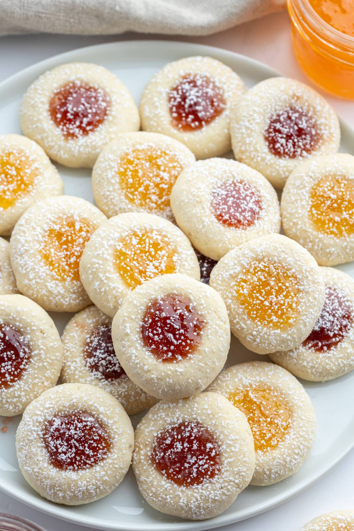 These soft and buttery Jam Thumbprint Cookies are filled with your favorite fruit jam and baked to golden perfection. A classic holiday cookie that’s easy, nostalgic, and perfect for gifting! jam thumbprint cookies dusted with powdered sugar