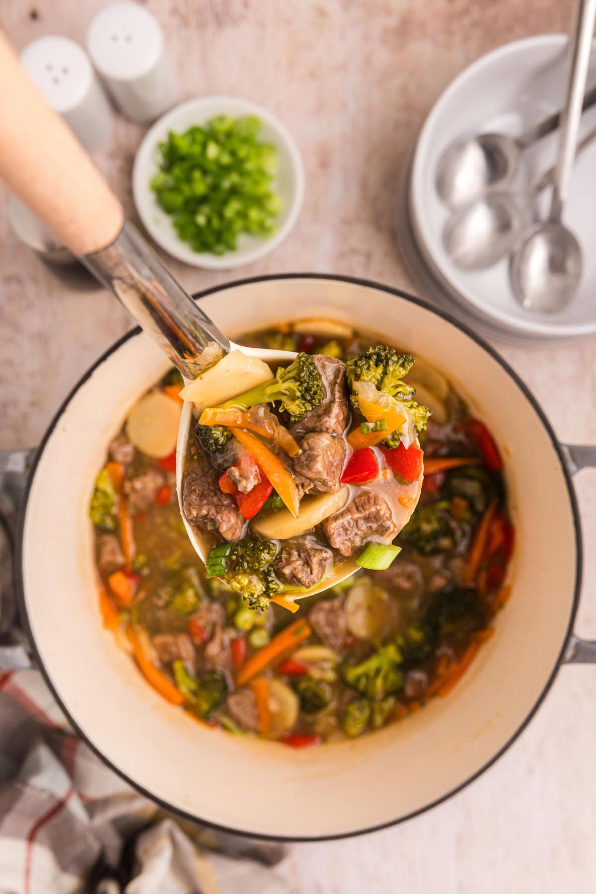 This Beef and Vegetable Stew is comfort food with a twist! Tender beef simmers in a savory soy-ginger broth with carrots, broccoli, red bell pepper, and water chestnuts. Perfect for cool nights and great for leftovers! ladle holding up some beef and vegetable stew