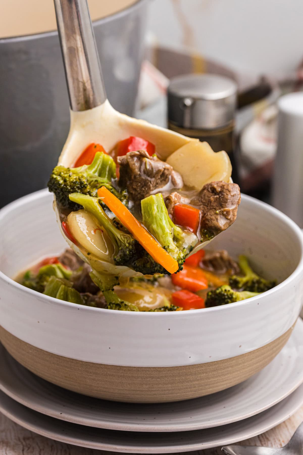 This Beef and Vegetable Stew is comfort food with a twist! Tender beef simmers in a savory soy-ginger broth with carrots, broccoli, red bell pepper, and water chestnuts. Perfect for cool nights and great for leftovers! ladle putting stew into bowl