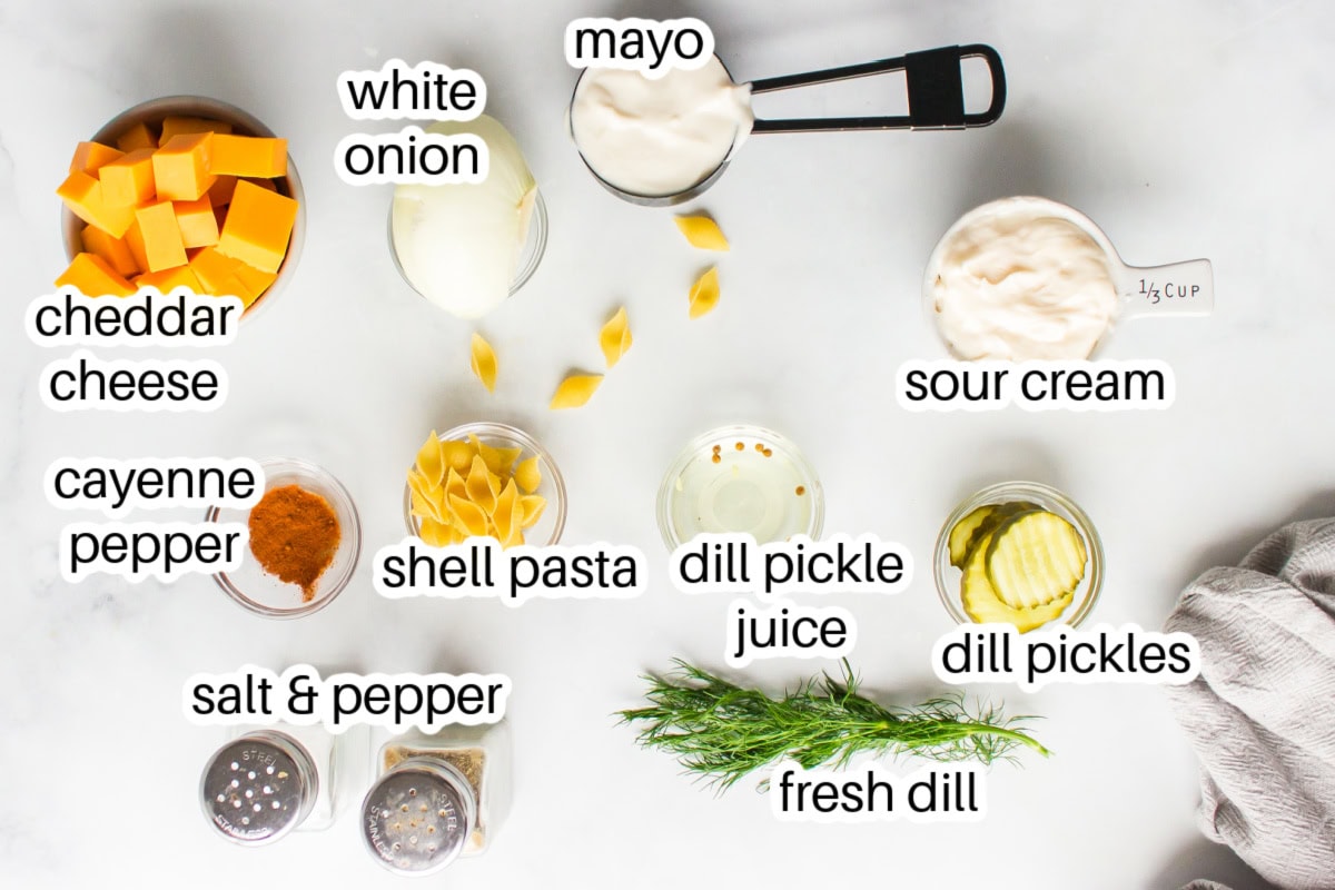 Dill Pickle Pasta Salad is the ultimate creamy, tangy side dish! Shell pasta is soaked in pickle juice, then tossed with cheddar, fresh dill, and a creamy dressing. Perfect for BBQs, potlucks, and summer parties! ingredients displayed for making dill pickle pasta salad