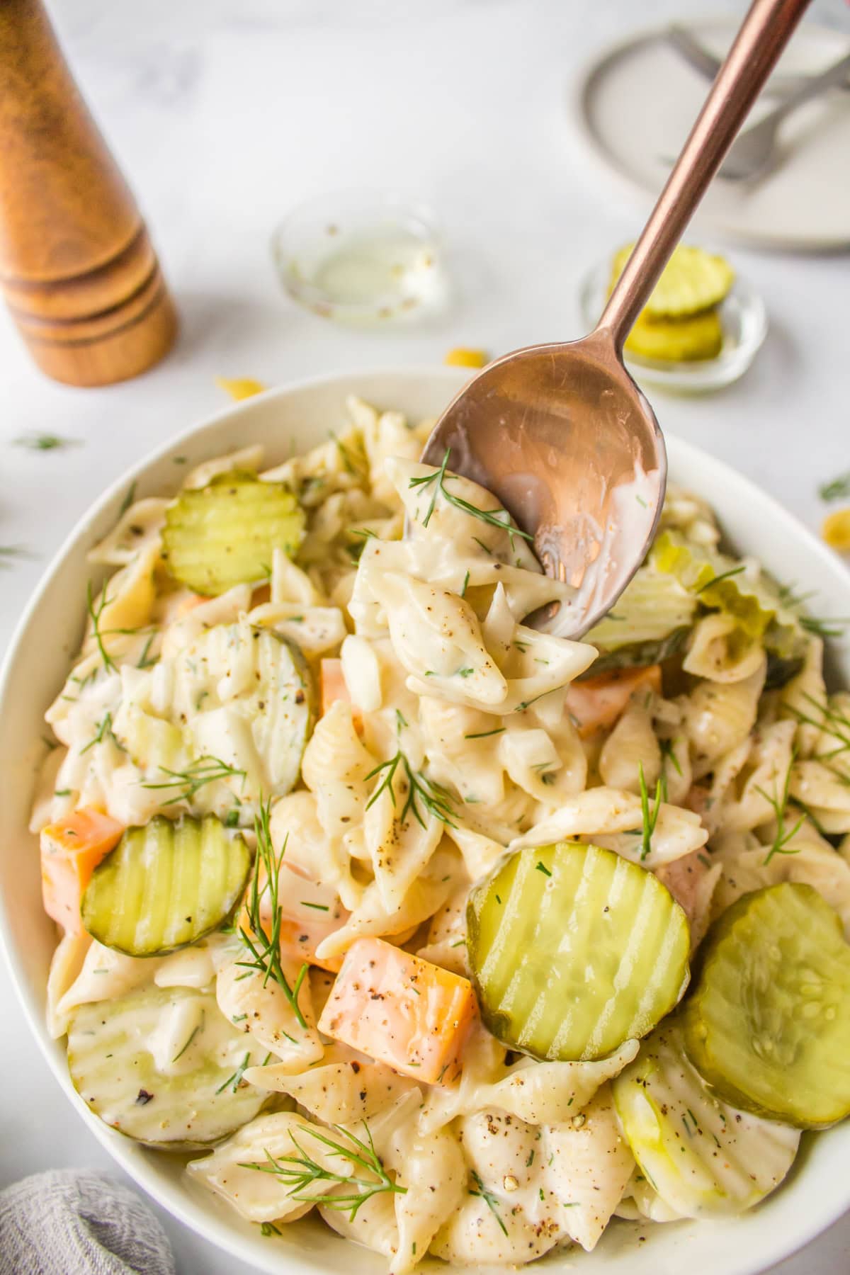 Dill Pickle Pasta Salad is the ultimate creamy, tangy side dish! Shell pasta is soaked in pickle juice, then tossed with cheddar, fresh dill, and a creamy dressing. Perfect for BBQs, potlucks, and summer parties! spoon in bowl of dill pickle pasta salad