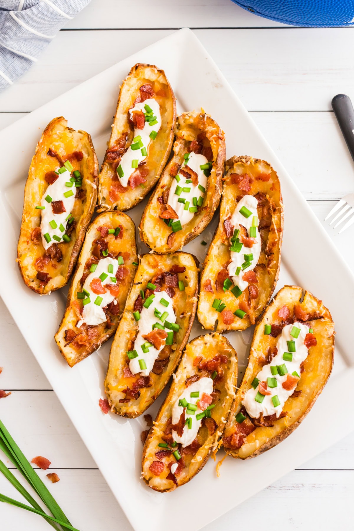 How to Make Potato Skins 🥔 Crispy baked potato shells brushed with buttery seasoning, filled with cheddar and bacon, then topped with sour cream and green onions. The BEST easy party appetizer! loaded potato skins on a platter