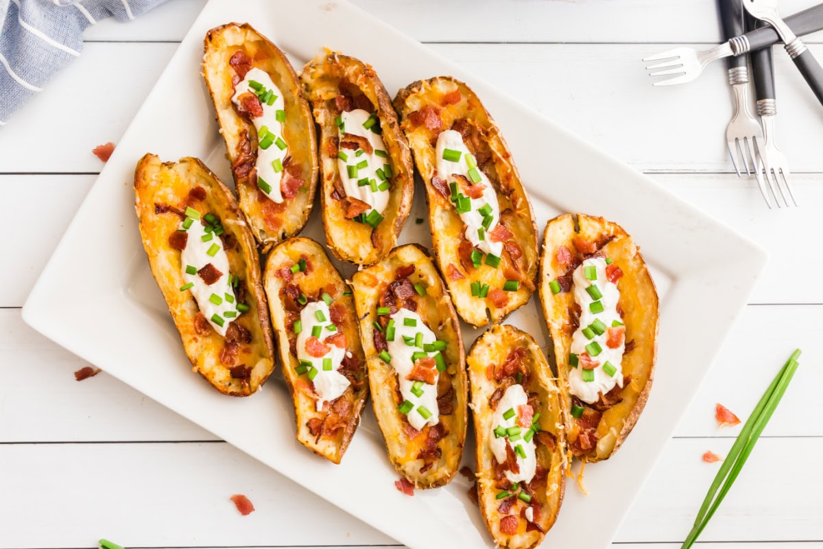 How to Make Potato Skins 🥔 Crispy baked potato shells brushed with buttery seasoning, filled with cheddar and bacon, then topped with sour cream and green onions. The BEST easy party appetizer! potato skins appetizer on platter