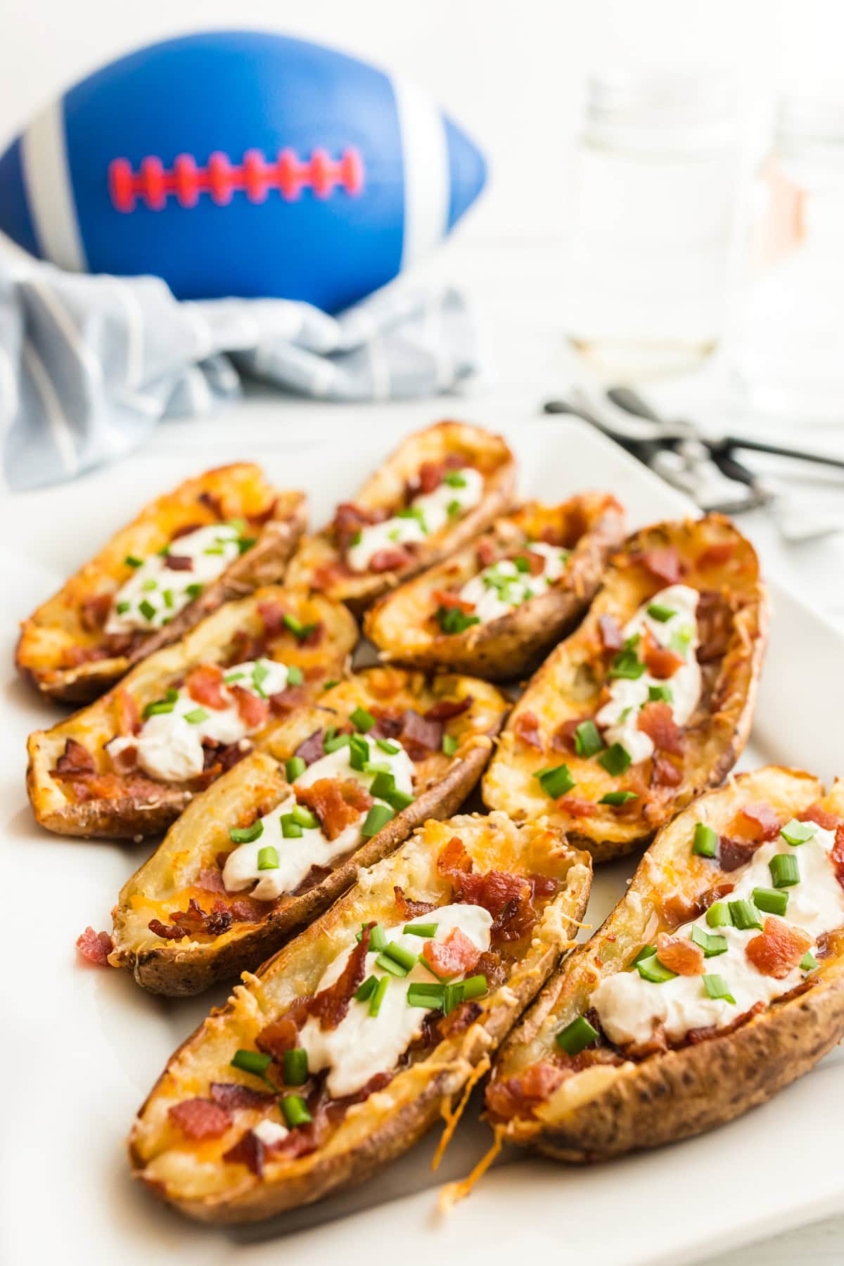 How to Make Potato Skins 🥔 Crispy baked potato shells brushed with buttery seasoning, filled with cheddar and bacon, then topped with sour cream and green onions. The BEST easy party appetizer! potato skins with a football in the background