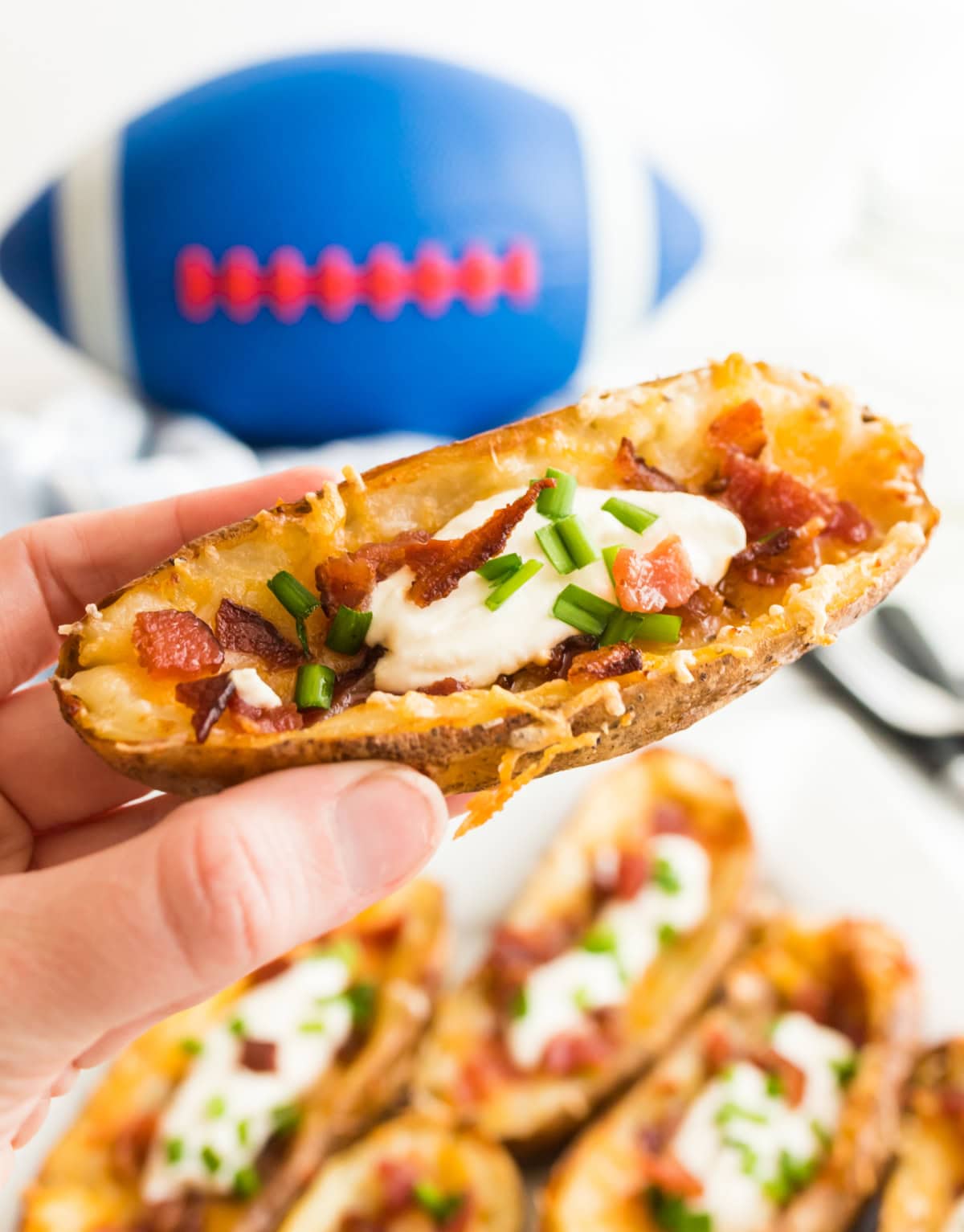 How to Make Potato Skins 🥔 Crispy baked potato shells brushed with buttery seasoning, filled with cheddar and bacon, then topped with sour cream and green onions. The BEST easy party appetizer! hand holding a loaded potato skin