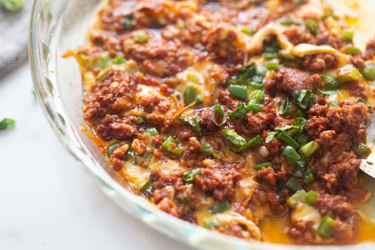 Queso Fundido Recipe 🧀🔥 Classic hot melted cheese dip baked with chorizo, jalapeños, and green onions. Ready in 30 minutes and perfect for parties, taco night, and game day! close up pan of queso fundido