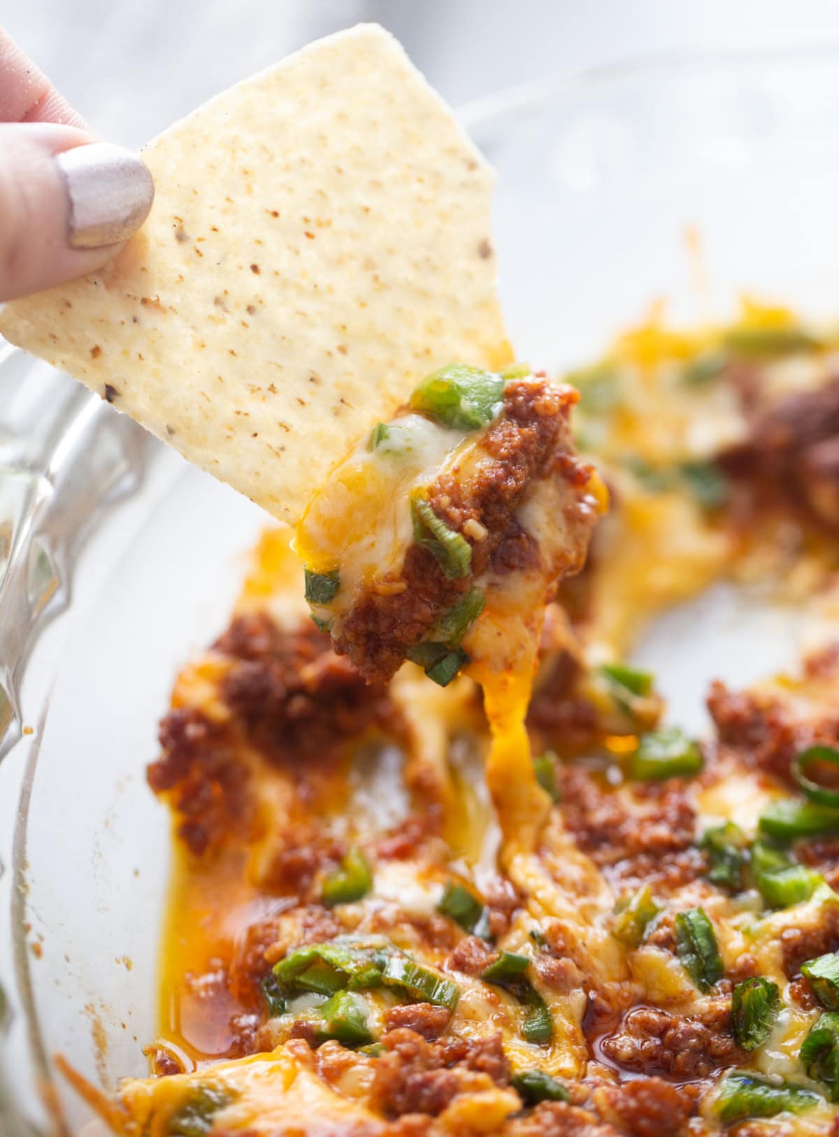 Queso Fundido Recipe 🧀🔥 Classic hot melted cheese dip baked with chorizo, jalapeños, and green onions. Ready in 30 minutes and perfect for parties, taco night, and game day! chip dipping into pan of queso fundido
