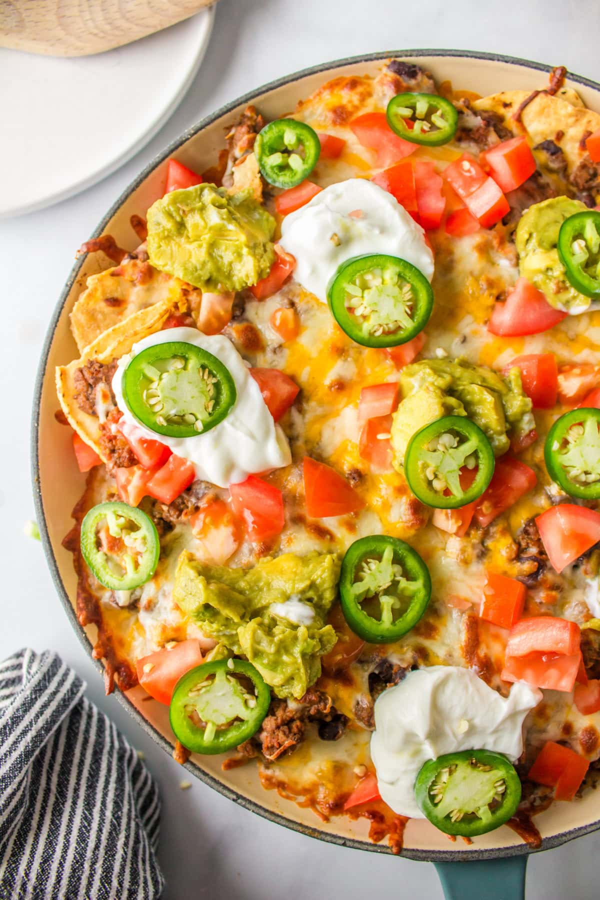 Skillet Nachos 🧀🌶️ The easiest way to make nachos! Tortilla chips topped with seasoned beef, Rotel, black beans, corn, and melty Colby-Jack cheese—add sour cream, guacamole & jalapeños! close up skillet nachos in skillet
