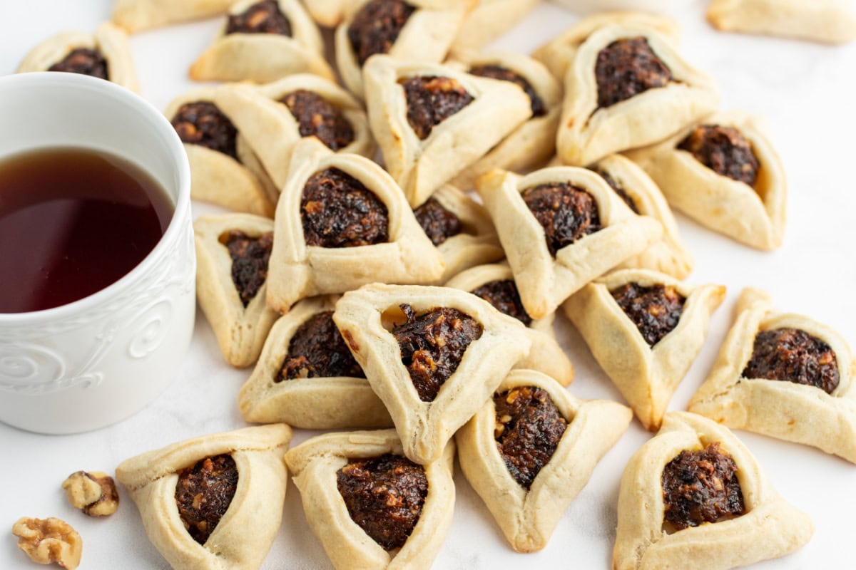 several hamantaschen laid out with cup of tea