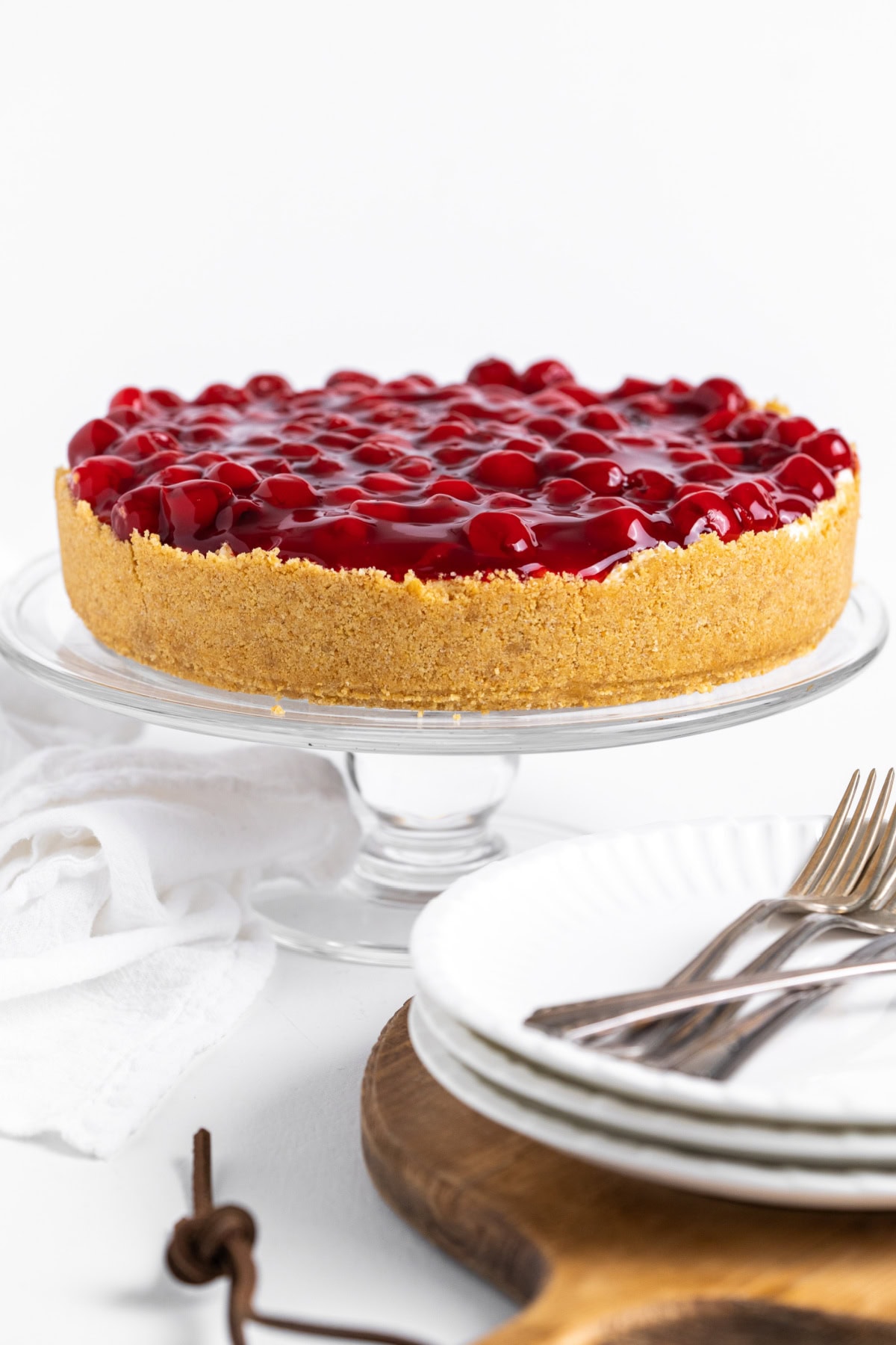 This easy No Bake Cherry Cheesecake has a buttery graham cracker crust, fluffy cream cheese filling, and sweet cherry topping. Perfect make-ahead dessert! no bake cherry cheesecake on cake stand