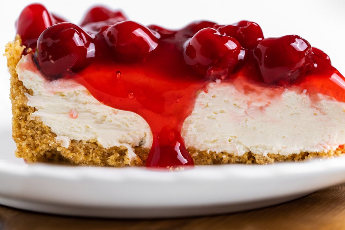 This easy No Bake Cherry Cheesecake has a buttery graham cracker crust, fluffy cream cheese filling, and sweet cherry topping. Perfect make-ahead dessert! close up slice of no bake cherry cheesecake